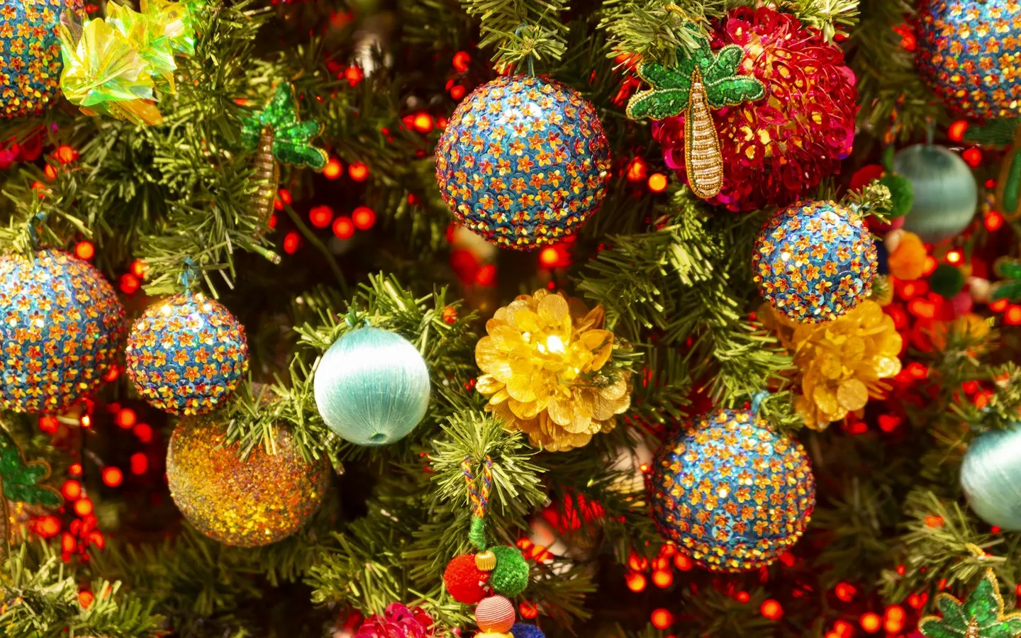 Bright glitter baubles in turquoise, gold, pink and red on a lit Christmas tree