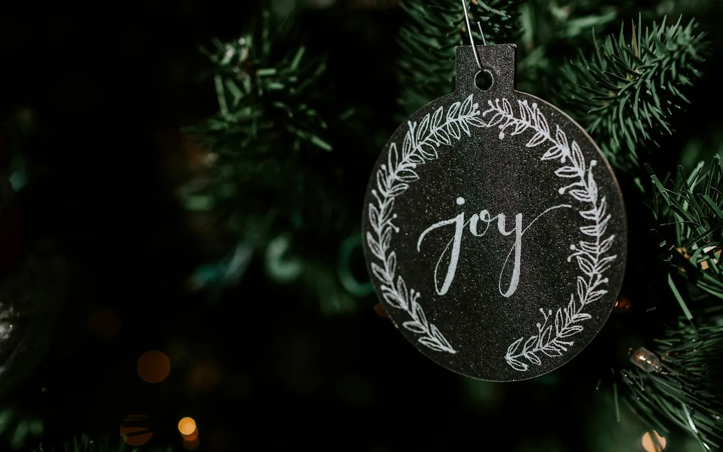 Hand-lettered joy ornament hanging on a dark fir branch