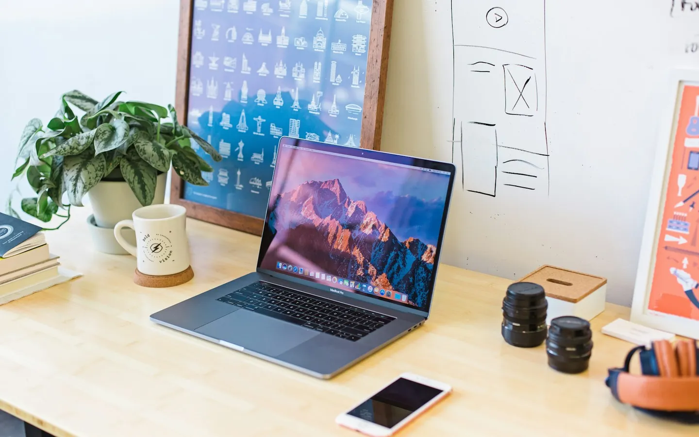 Tidy desk with a laptop, a plant, a mug and sketches pinned to the wall