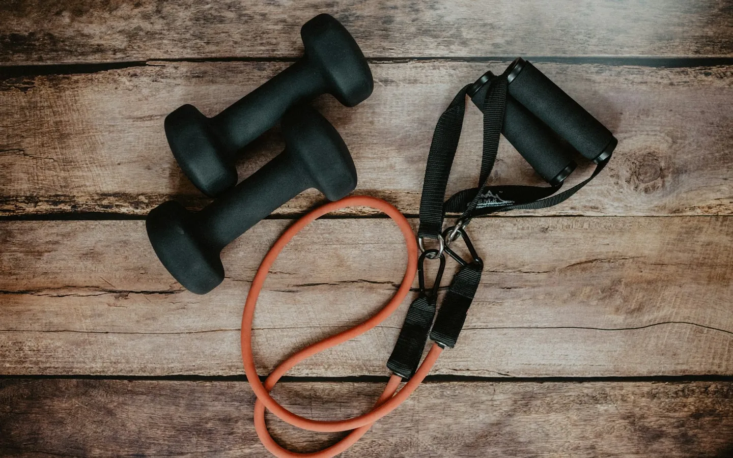 Two black dumbbells and an orange resistance band on rustic wood