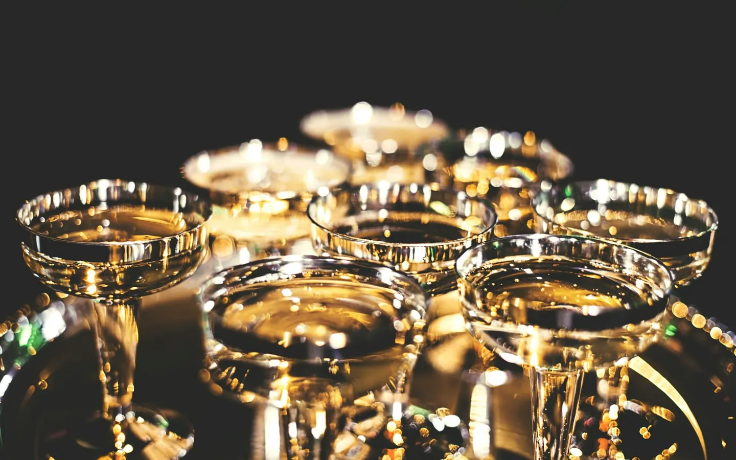Rows of gold-rimmed coupe glasses glowing in warm light on a dark table
