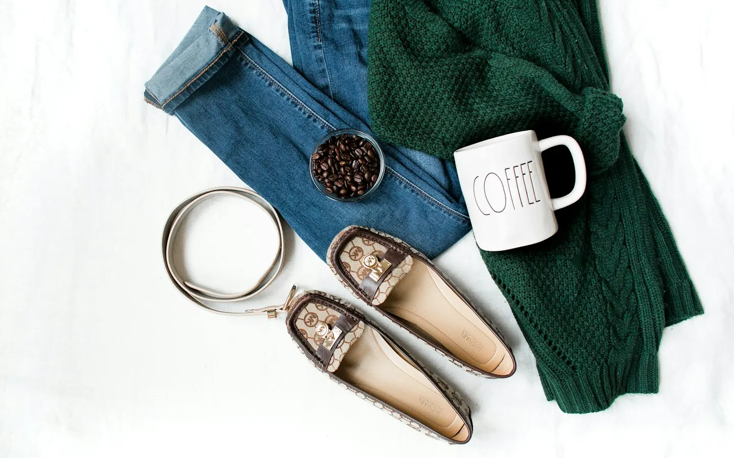 Flat lay of jeans, a green knit sweater, brown leather flats, a belt and a white mug